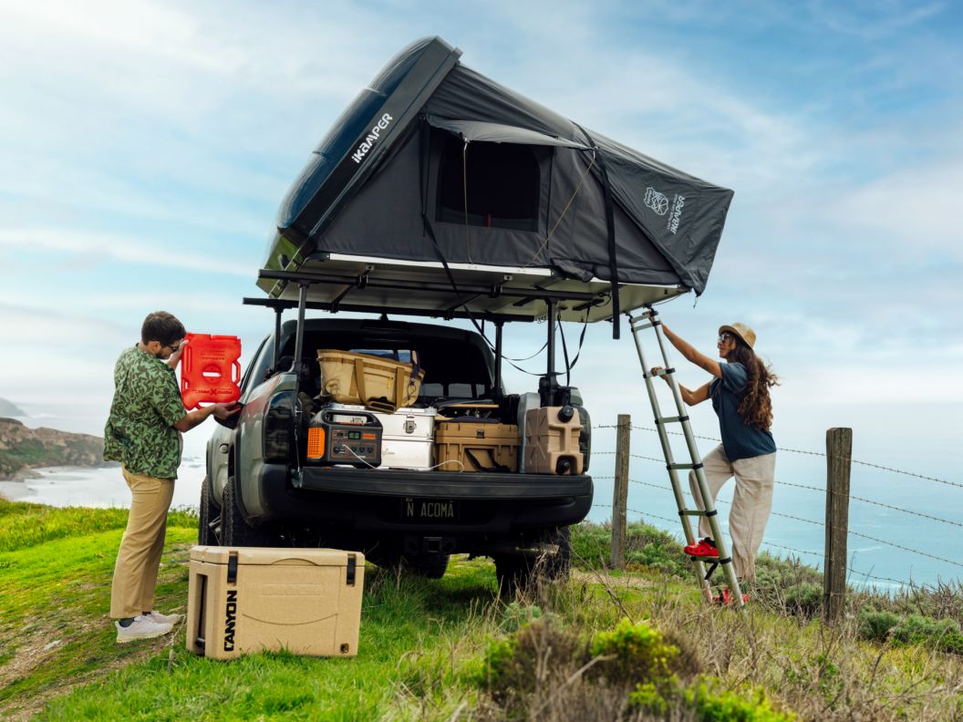 Two people camp near the ocean in a truck with a rooftop tent. 