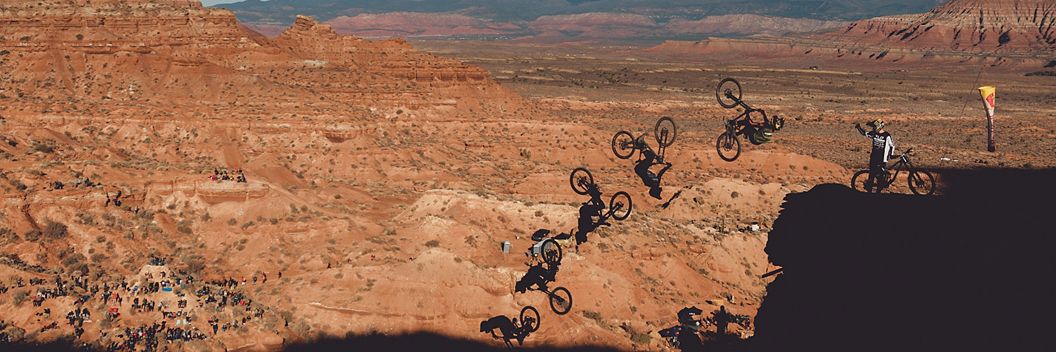In a multiplicity photograph a Red Bull rider is shown performing a trick off a red rock cliff in the desert. 