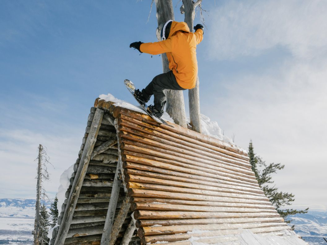 A snowboarder stalls on top of a wooden quarter pipe.