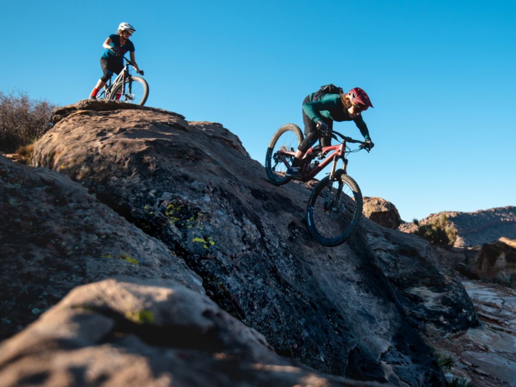 A woman rides a mountain bike on a narrow spine of red rocks.