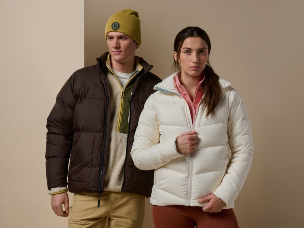 Two models wearing a brown puffer jacket and a white puffer jacket against a tan background.