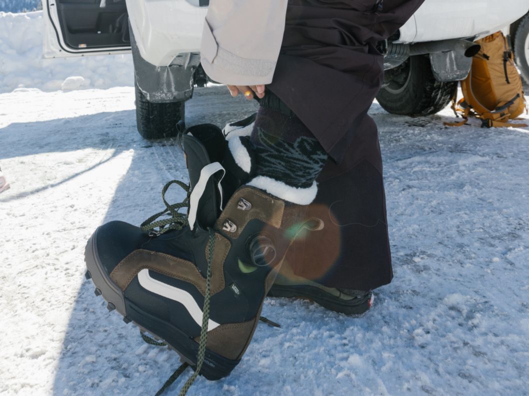 Snowboarder putting boots on in parking lot. 