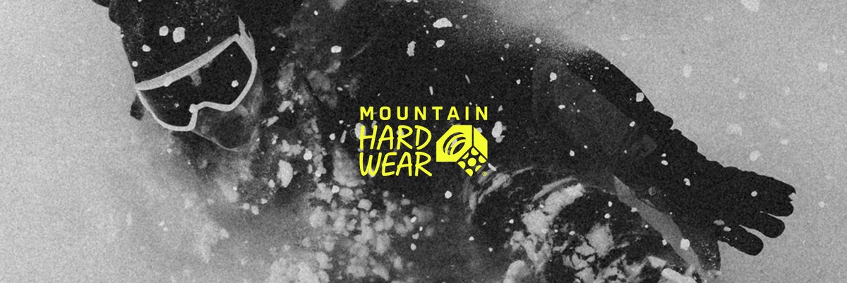 A skier walks between two large boulders. The word “Mountain Hardwere” is over them.