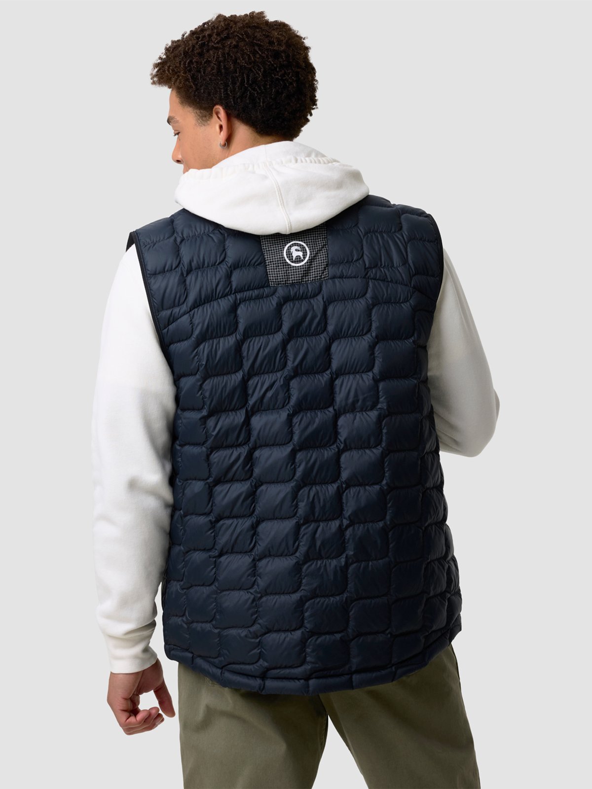 Men's navy quilted puffer vest with white hooded hoodie and olive pants featuring box-stitch pattern and branded chest logo.