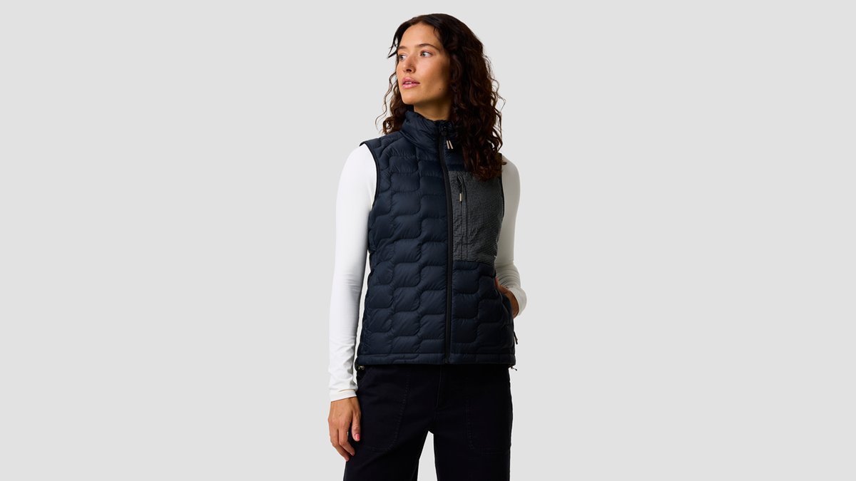 A woman wears the LT ALLIED Down Vest against a grey background