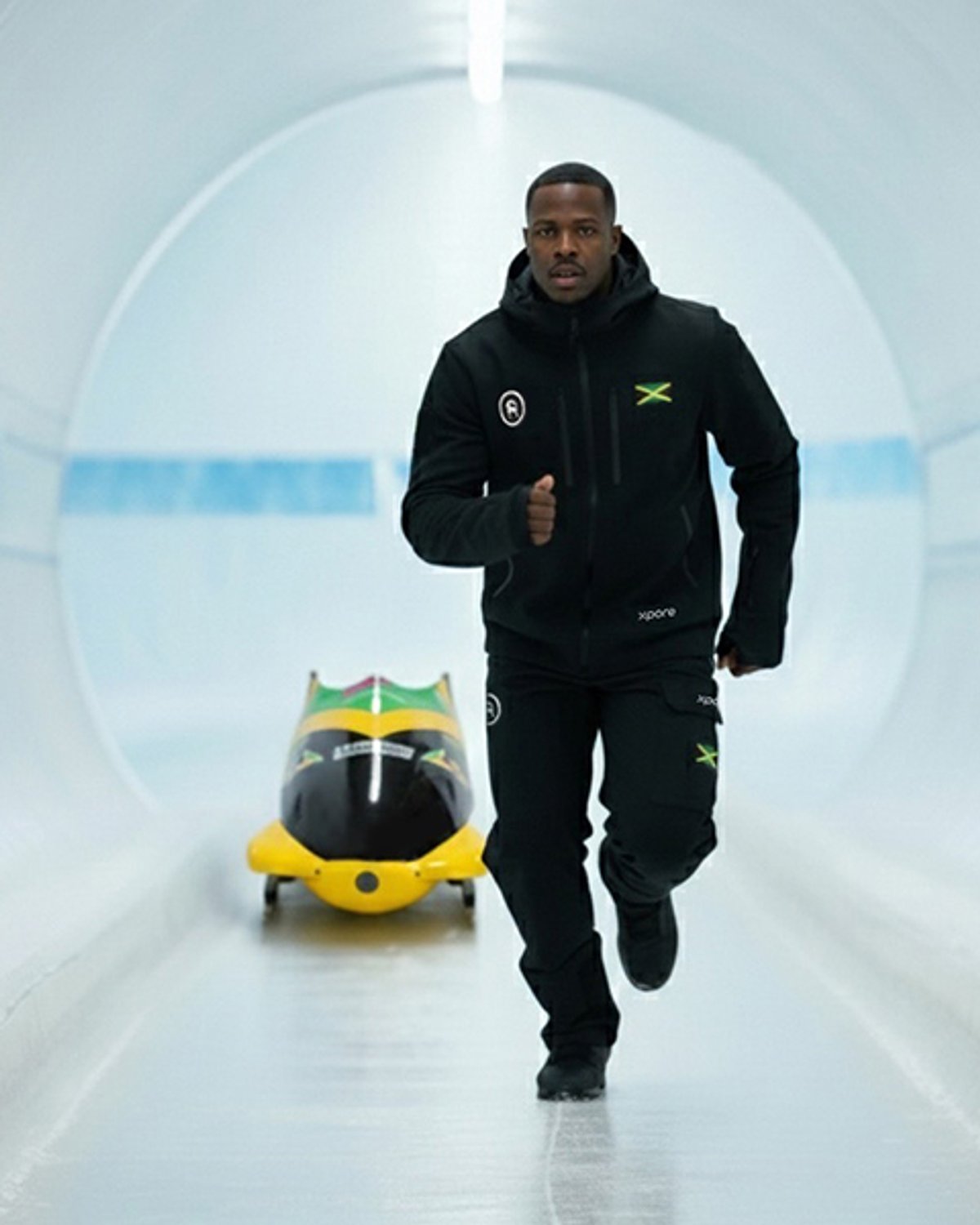 Jamaica bobsleigh team member on bobsleigh track with bobsled in the background.