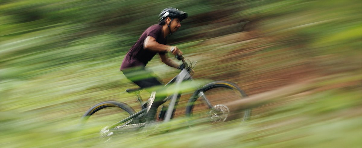 High-speed panned shot of mountain biker racing full-suspension electric mountain bike across open green trail