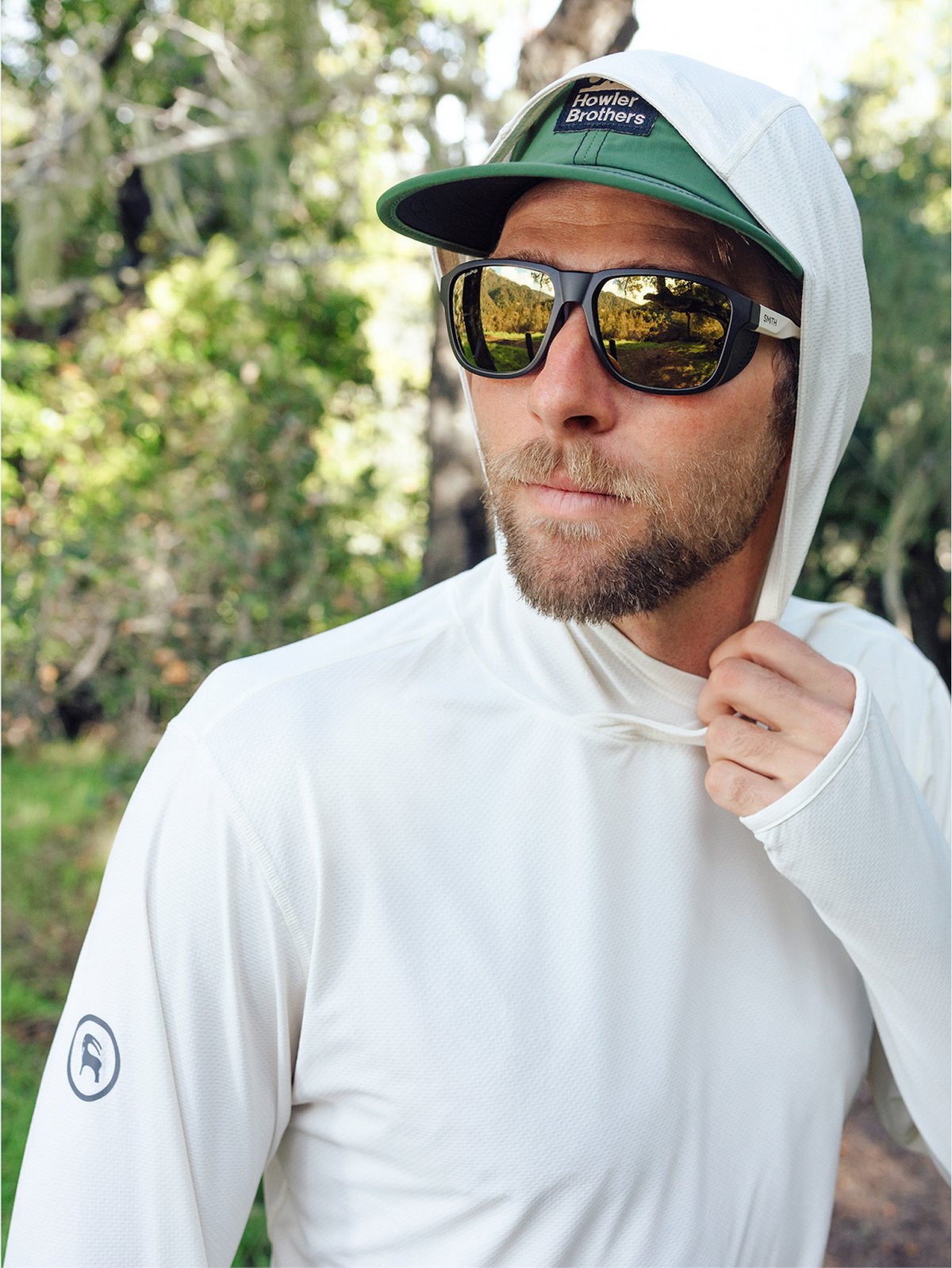 A man wearing sun glasses and a sun hoodie looks off.