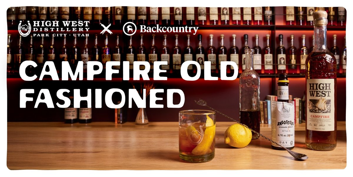 A bar countertop displays ingredients for a cocktail, including a bottle of High West Campfire whiskey, a bottle of Angostura aromatic bitters, a lemon, a mixing spoon, and a glass filled with an old fashioned cocktail, with a background of shelves lined with liquor bottles. The top of the image has the text “Campfire Old Fashioned” below the High West Distillery and Backcountry logos.