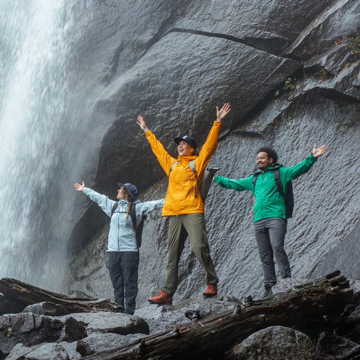 A group of hikers wearing Helium Rain Jackets pose triumphantly in front of a waterfall
