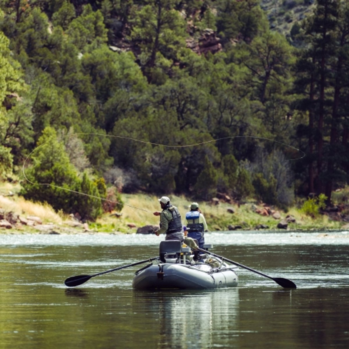 Fly fisher rows up the river in an inflatable raft. 