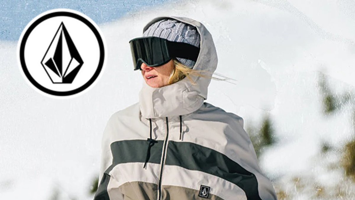 A person wearing a Volcom winter jacket, beanie, and goggles stands against a snowy background.