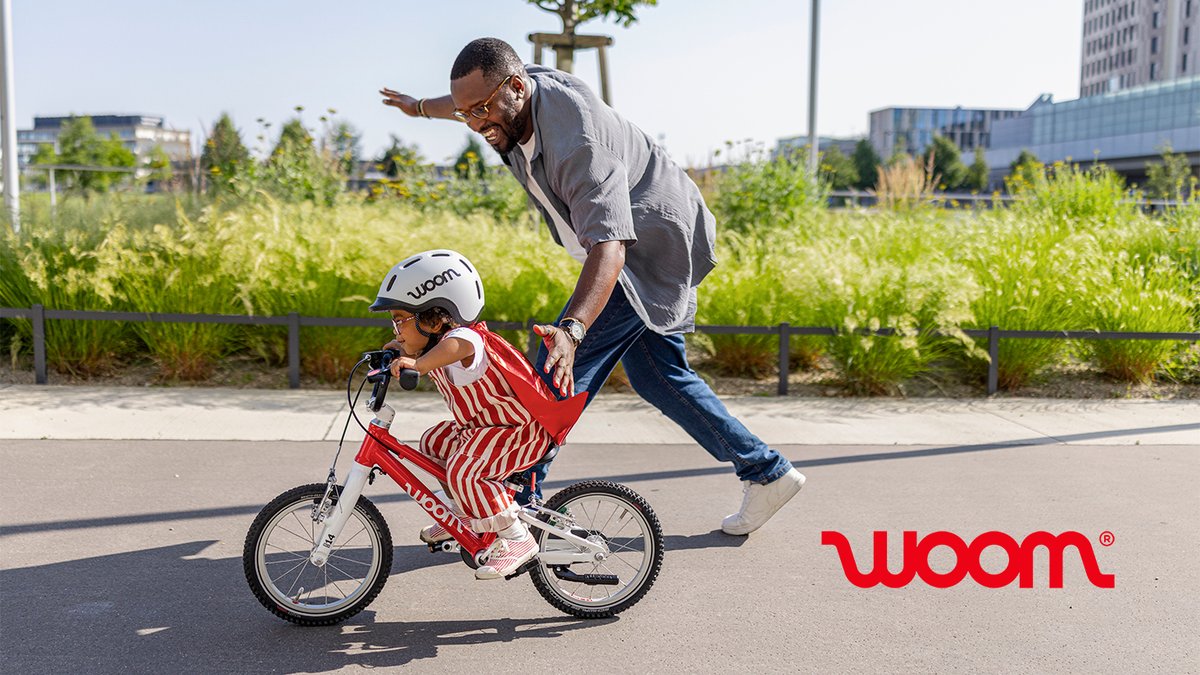 Tiny rider on a balance wearing superhero cape being pushed by an adult running alongside them.