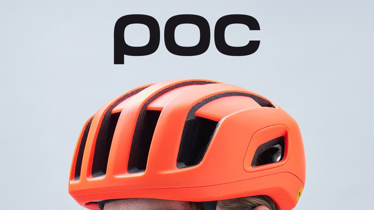 A close-up view of a bright orange POC cycling helmet worn by a rider against a plain grey background.