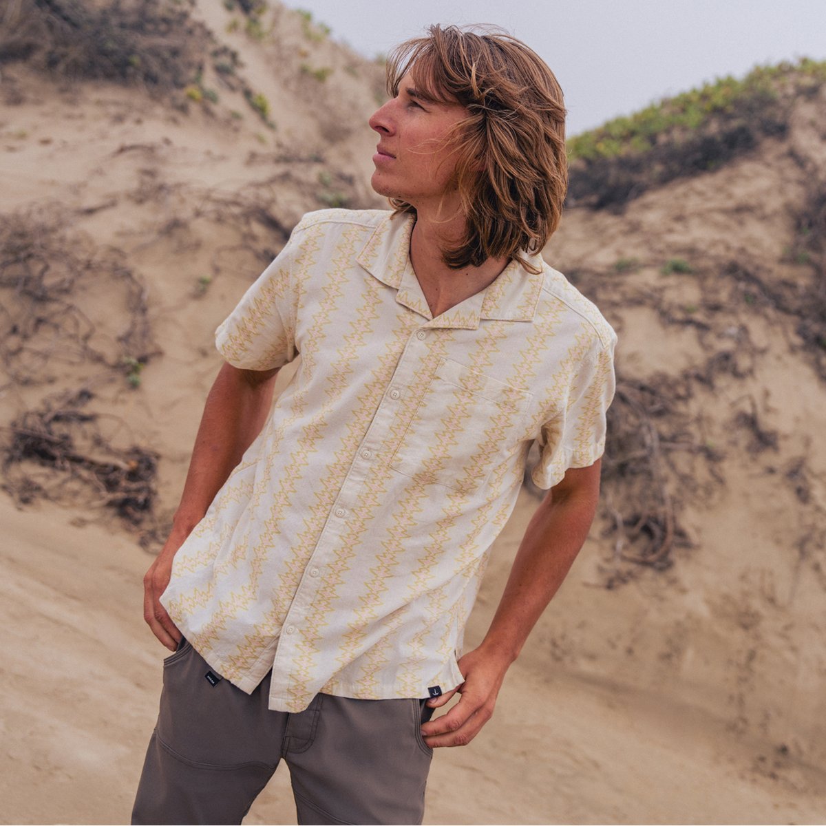 A man wears a prAna button down and Stretch Zion pants against a sandy outdoor landscape.