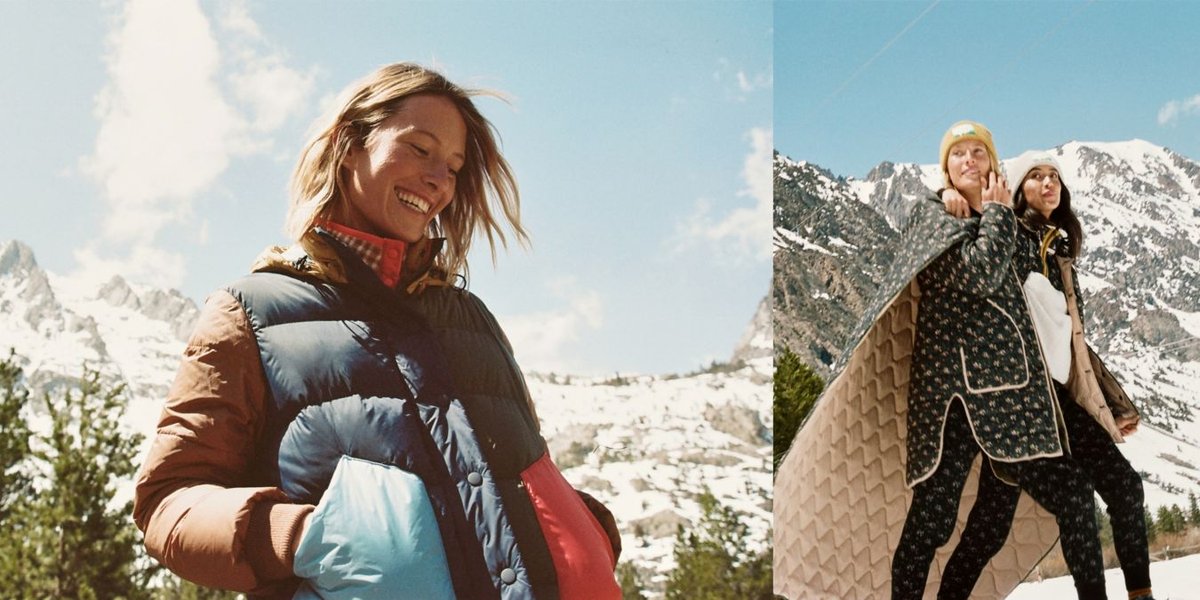 Two women wearing floral print long underwear and colorblocked puffy vests walk in a snowy field.