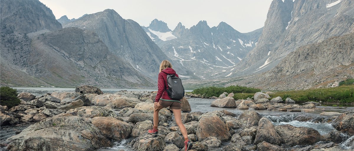 Person wearing Coalatree Trailhead Shorts hiking over rocky river crossing with mountains in the background.