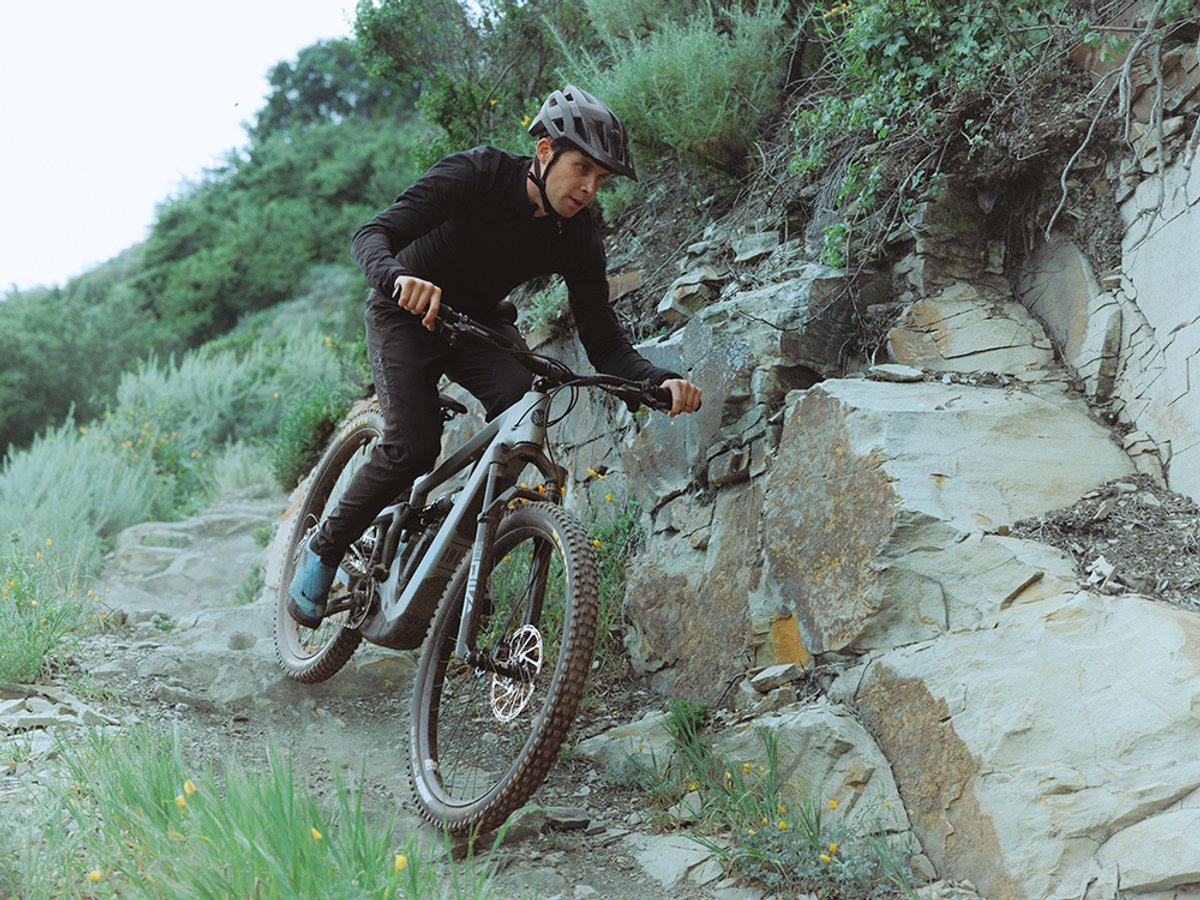 Rider wearing MTB helmet and long sleeve jersey navigating full-suspension electric mountain bike down rocky trail