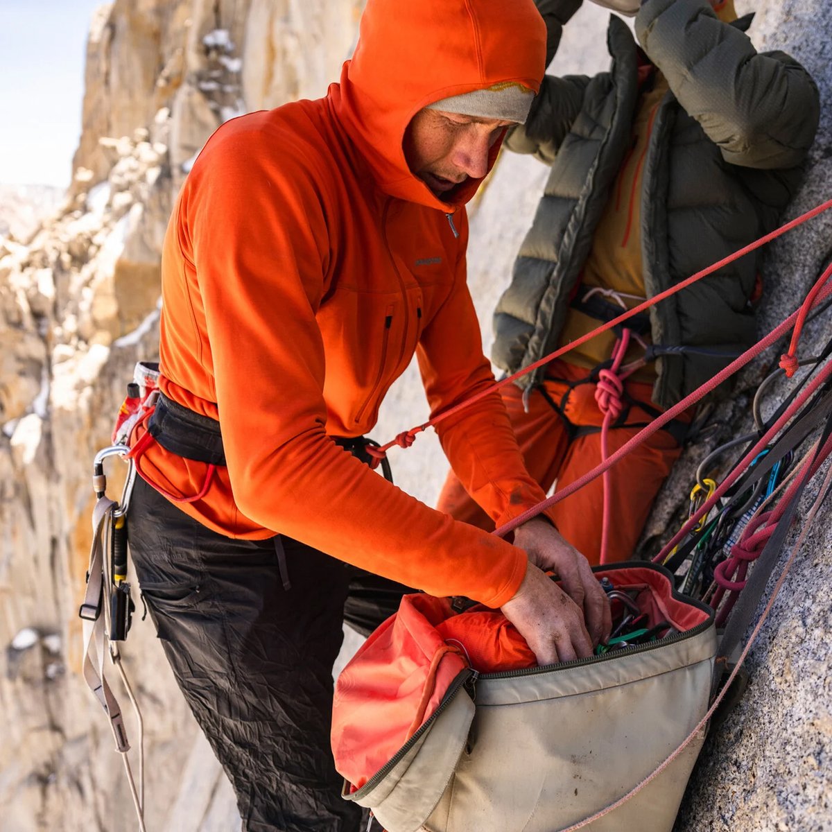 A man wearing a Patagonia R1 hoodie searches through a bag of cams.