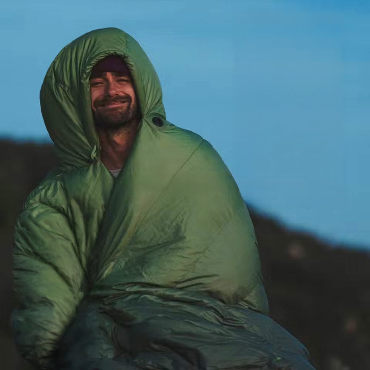 A man watches the sun rise, warm in his Marmot Wraptor sleeping bag. 