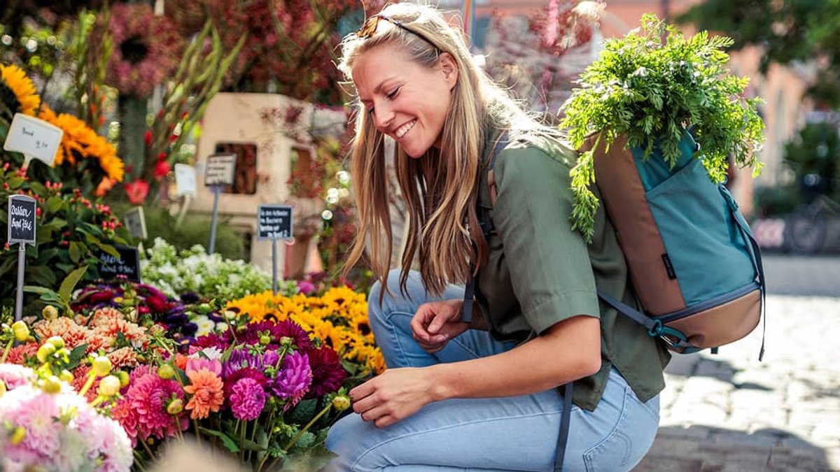 A woman wearing an Osprey Daylite pack kneels down to pick out some flowers from a street vendor. 