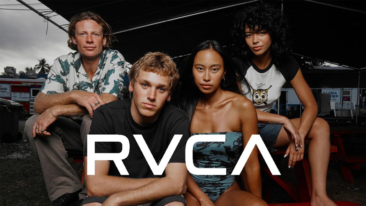 A diverse group of five people poses together outdoors under a black canopy with tropical scenery in the background, wearing casual summer clothing and the RVCA brand logo displayed prominently.