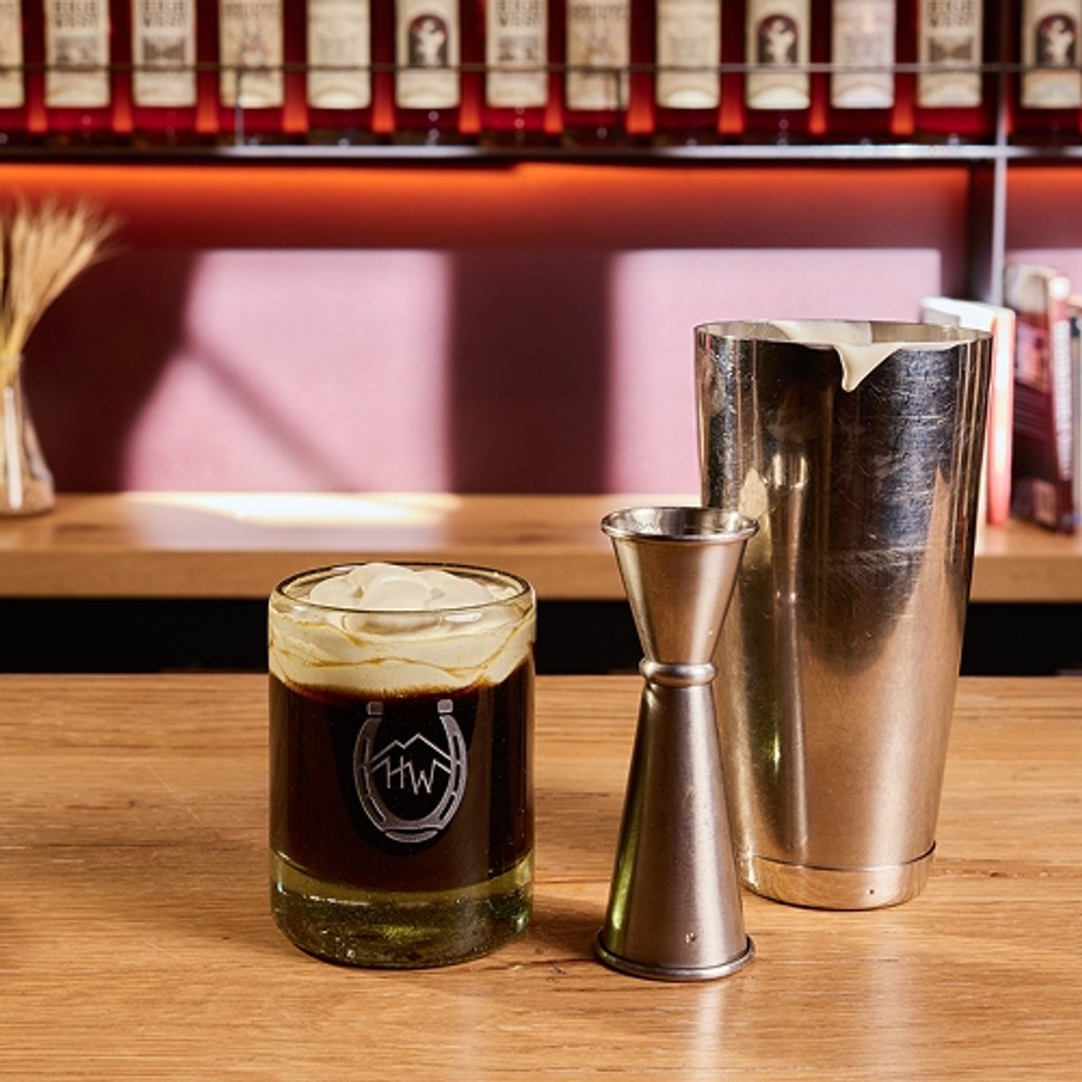 A bar countertop displays a glass of coffee cocktail topped with cream, a bottle of High West Bourbon, a cocktail shaker, and a bottle of simple syrup, against shelves filled with liquor bottles. Large text reads: "Cowboy coffee," and the top corner features the High West Distillery and Backcountry logos.