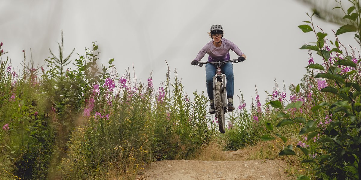 Mountain biker getting air on a trail surrounded by wildflowers.