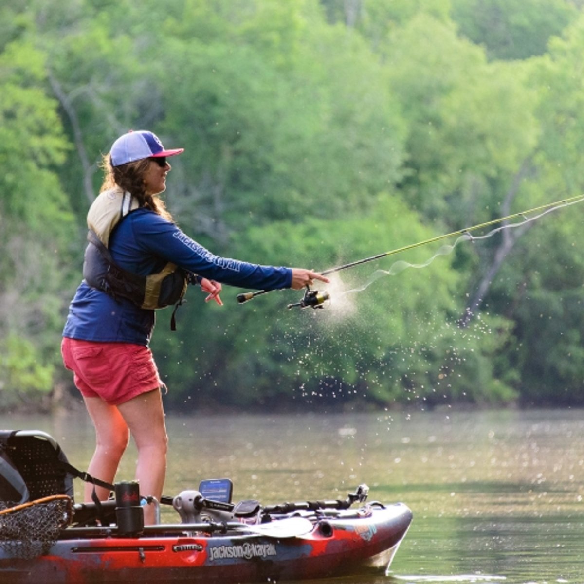 An angler casts their rod while standing in a fishing kayak. 