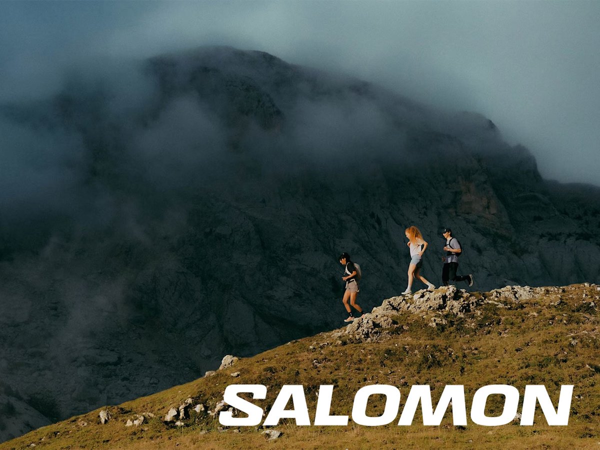 Three runners running down a rocky hill with a cloudy mountain in the background and "Salomon" logo overlay.