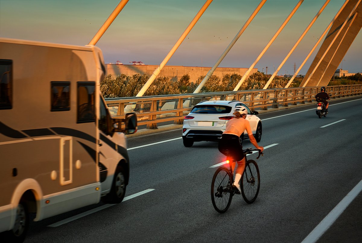 Cyclist riding in traffic with bright rear bike light illuminated at sunset
