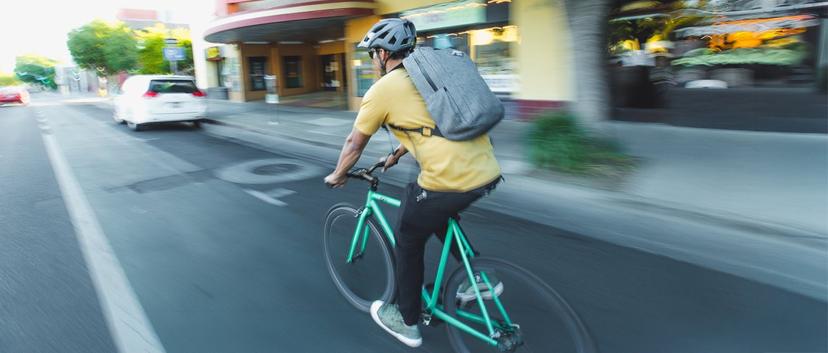 Person commuting via bicycle through a city wearing Coalatree Compass Backback.