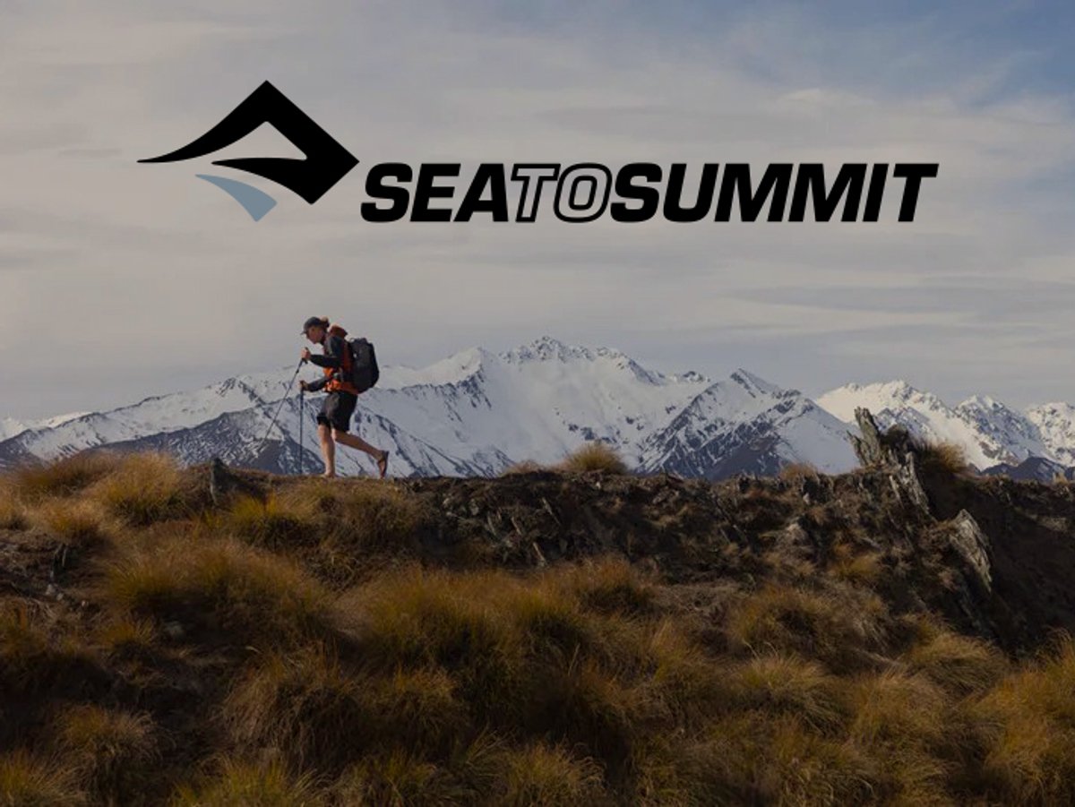 A lone hiker with a backpack and trekking poles walking along a grassy ridge with snow-capped mountains behind them; the Sea to Summit logo is at the top.
