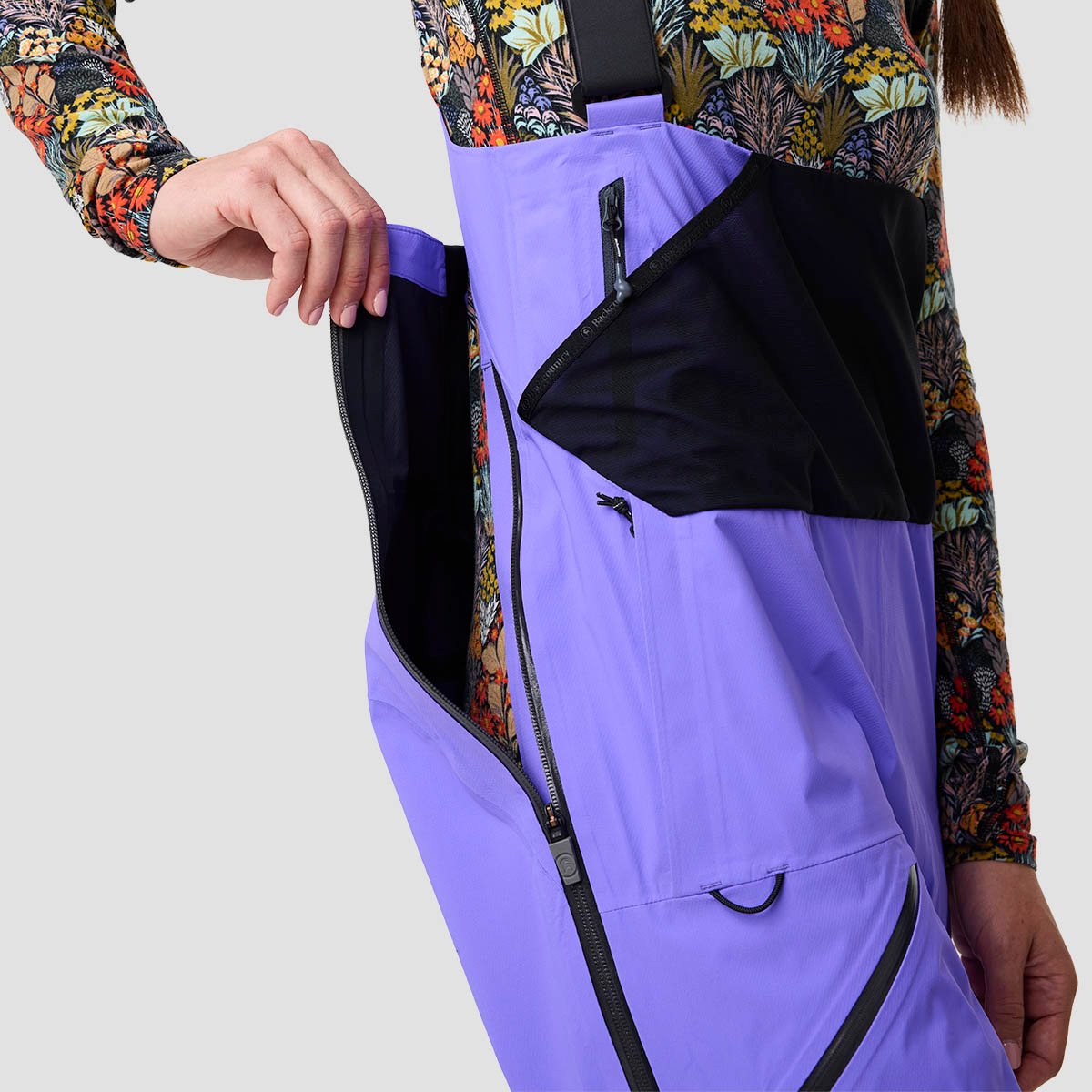 Person wearing ski bibs unzipping outer zip to show drop-seat bathroom access.