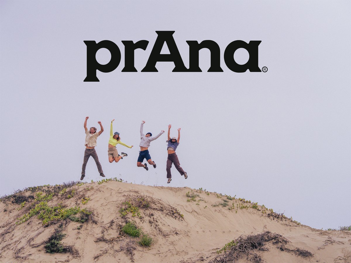 Four people jumping for joy on top of a sand dune against an overcast sky; the "prAna" logo is centered at the top