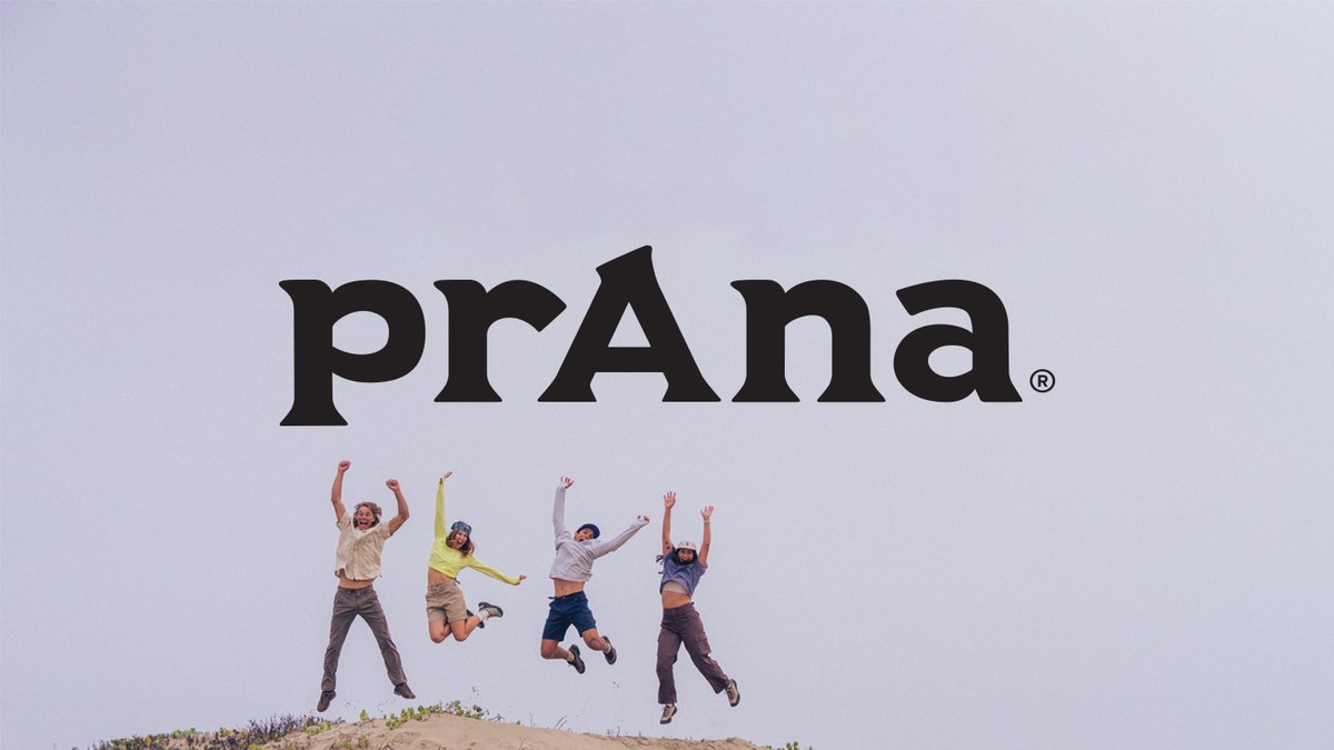 Four people jumping for joy on top of a sand dune against an overcast sky; the "prAna" logo is centered at the top
