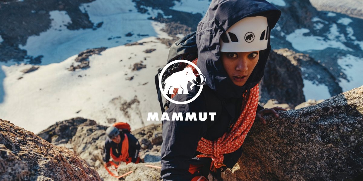 A woman in a helmet climbs a rocky, snowy mountain, with an orange rope over her shoulder.