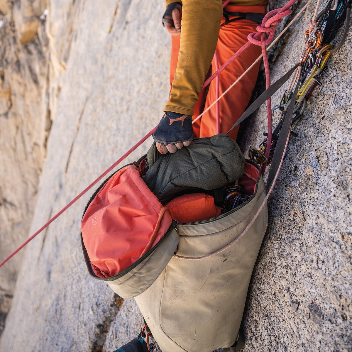 Climber accessing gear while on steep granite face during alpine rock climb.