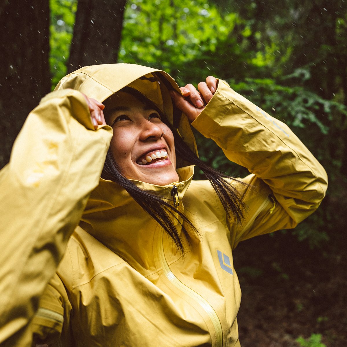 A woman adjusting the hood of her yellow rain shell.