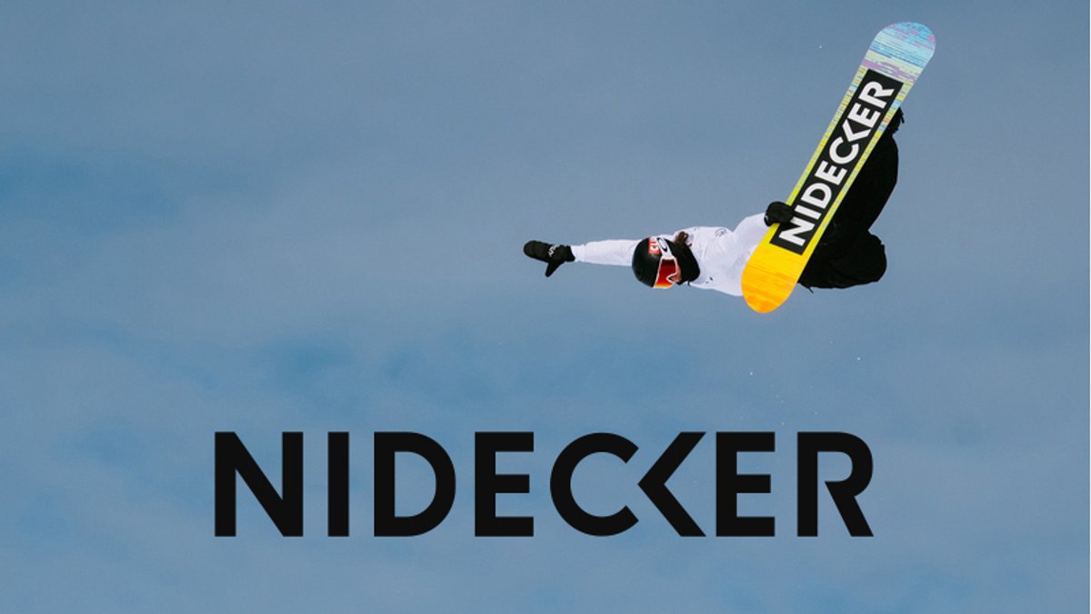 Snowboarder performing aerial trick with Nidecker snowboard above snowy terrain with Nidecker logo
