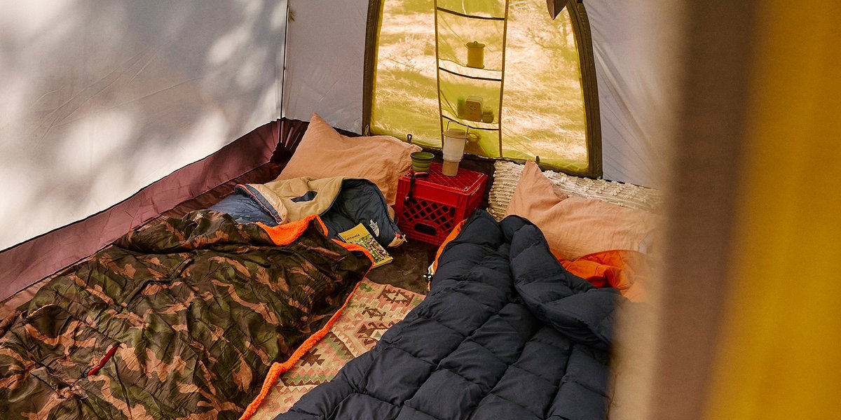 The interior of a very cozy tent, with two sleeping bags and a overturned milk crate with a lantern on top.