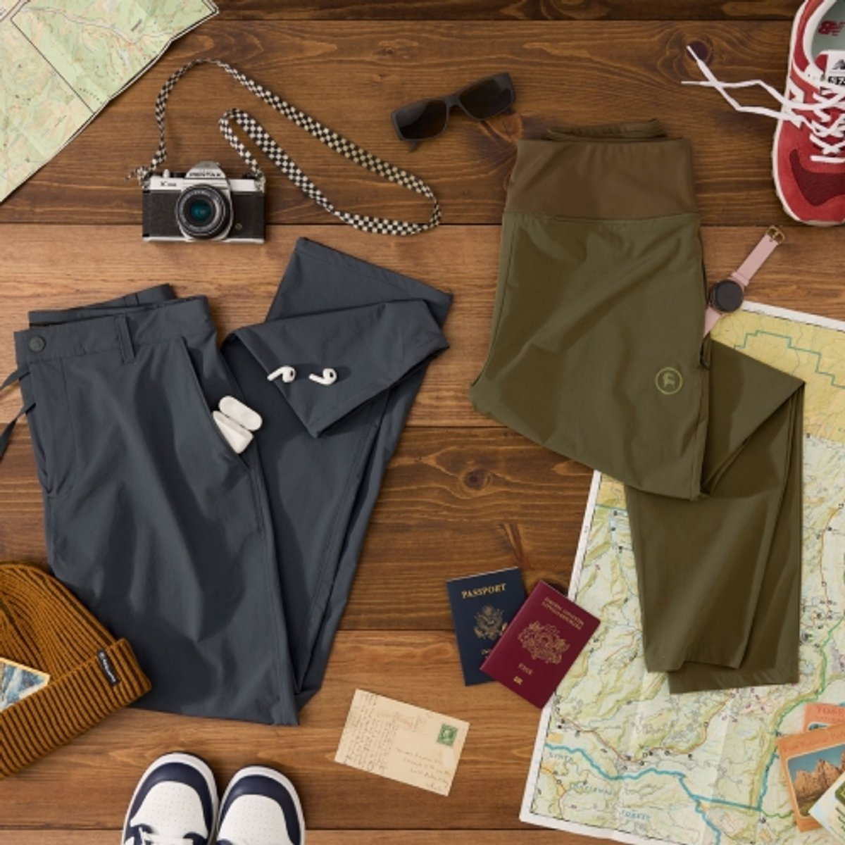 A few pairs of travel pants staged on a wooden background with travel accessories. 