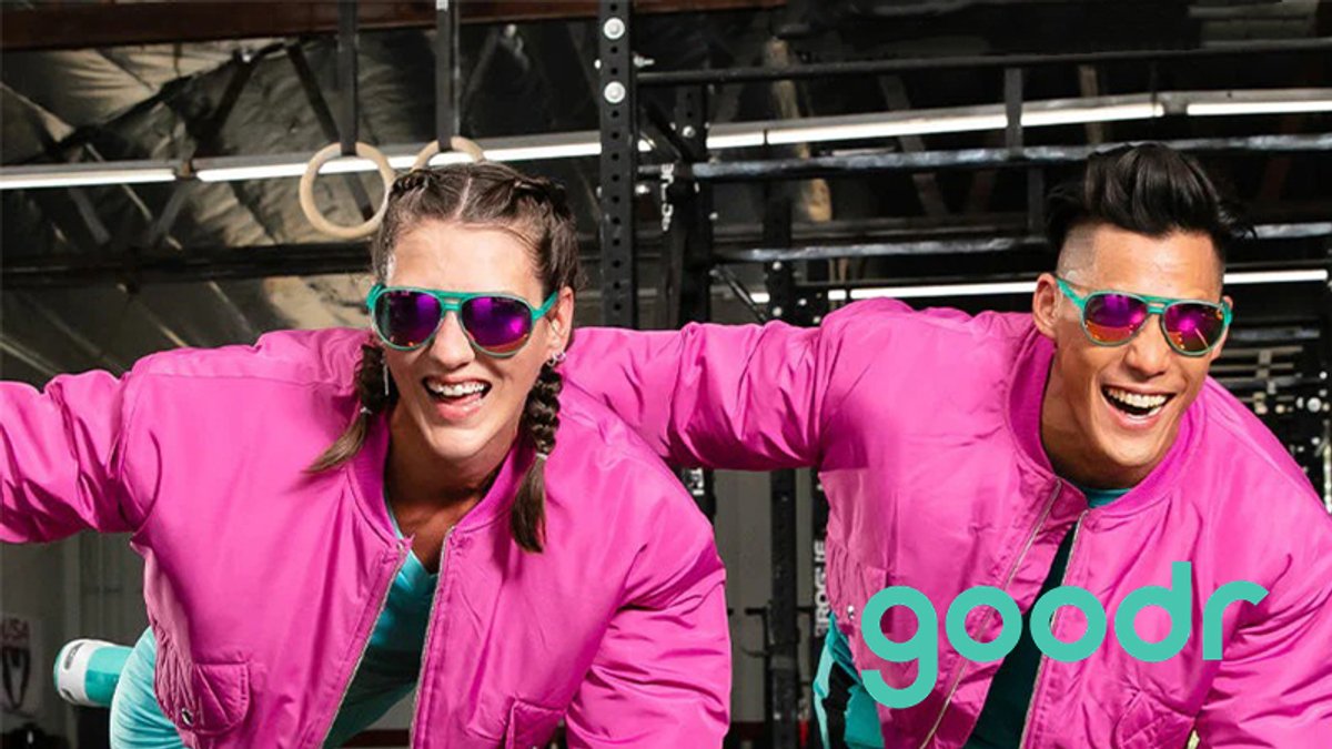 Two people wearing matching bright pink jackets and colorful sunglasses pose together in a gym setting.