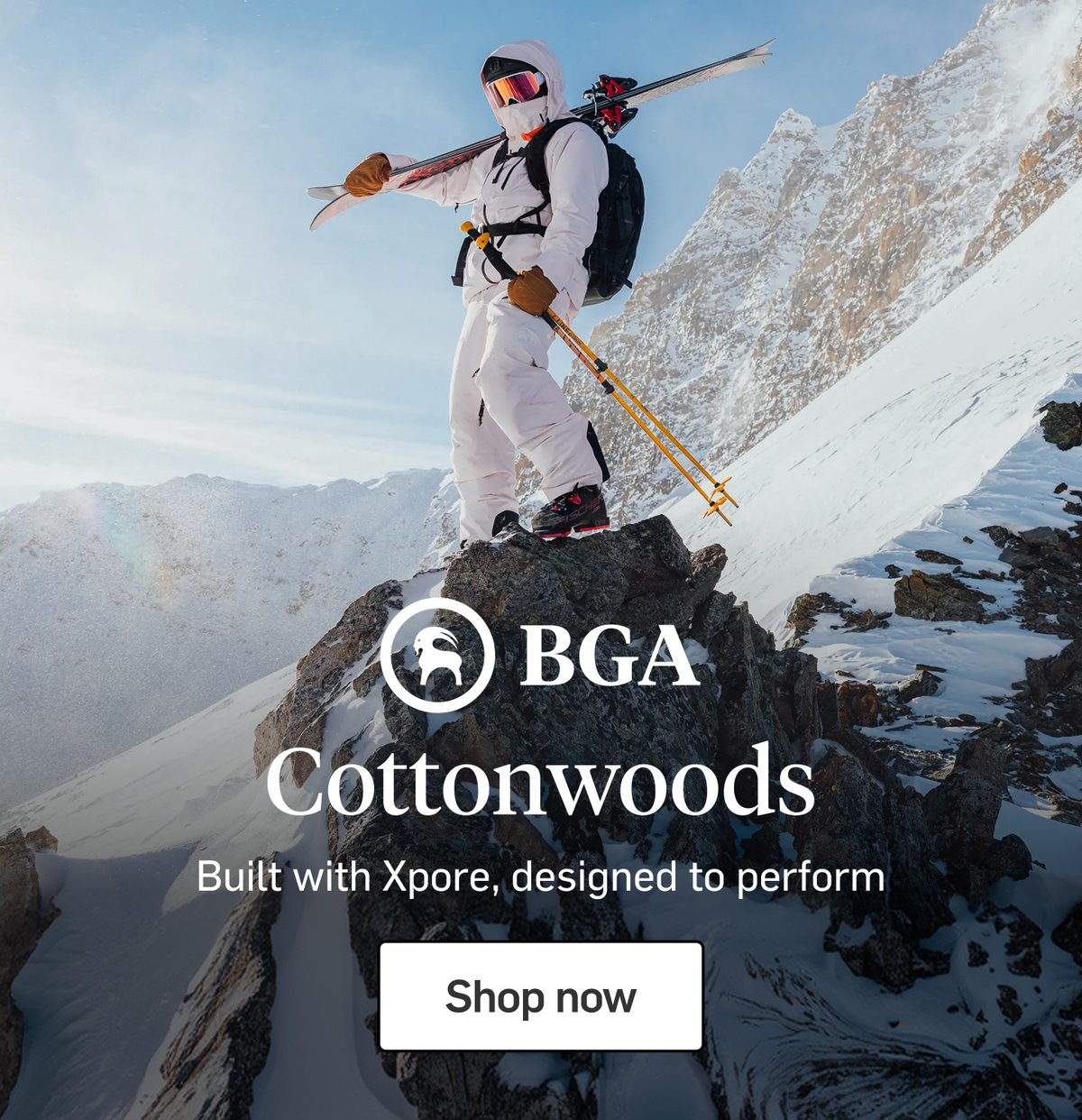 Skier in a white suit standing on a rocky alpine summit with skis over one shoulder, featuring the BGA logo.