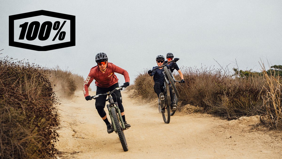 A group of mountain bikers ride joyfully down a trial, with the 100% logo overlaid on top.