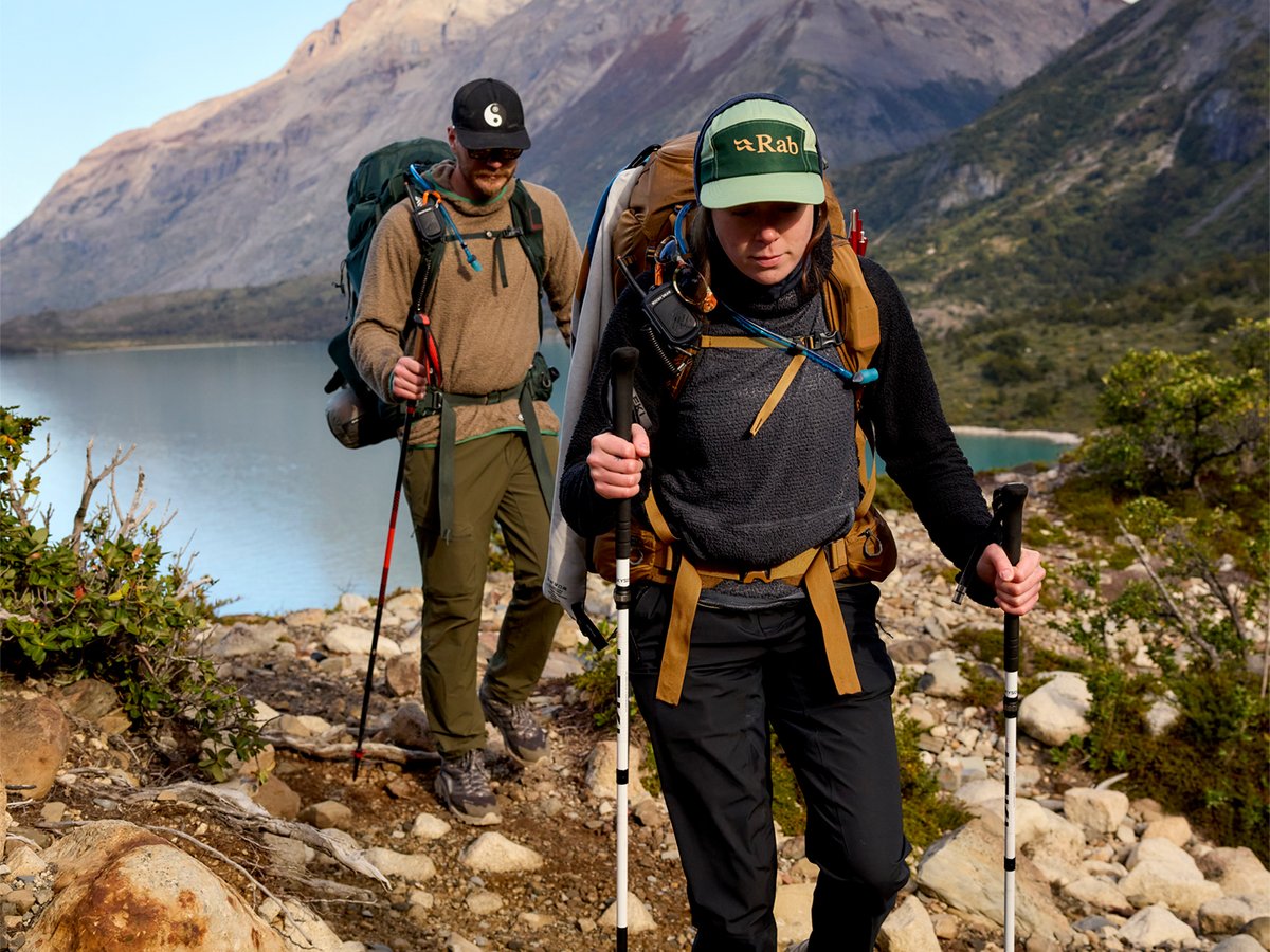 Two backpkers hiking on a mountain trail with a lake in the background.