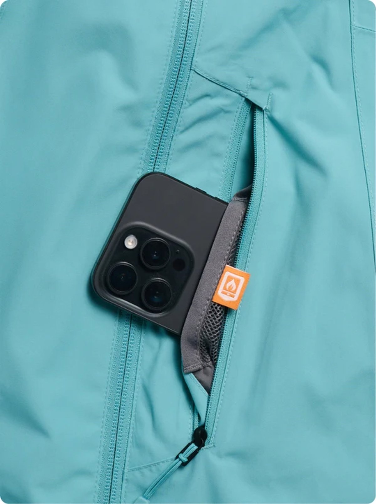 Black smartphone with triple camera setup secured in a gray protective case attached to a turquoise zippered jacket pocket with orange brand label.
