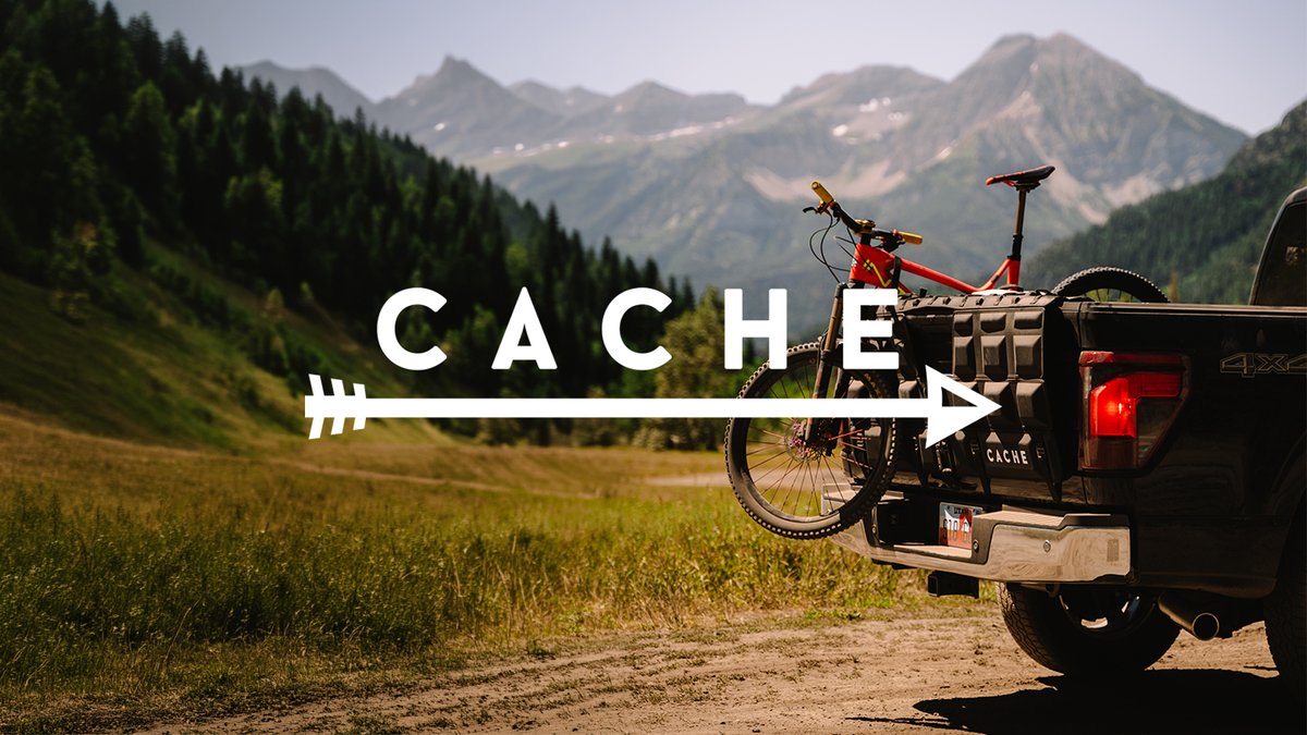 Cache brand logo overlaid on truck parked with tailgate pad and bike with mountains in the background