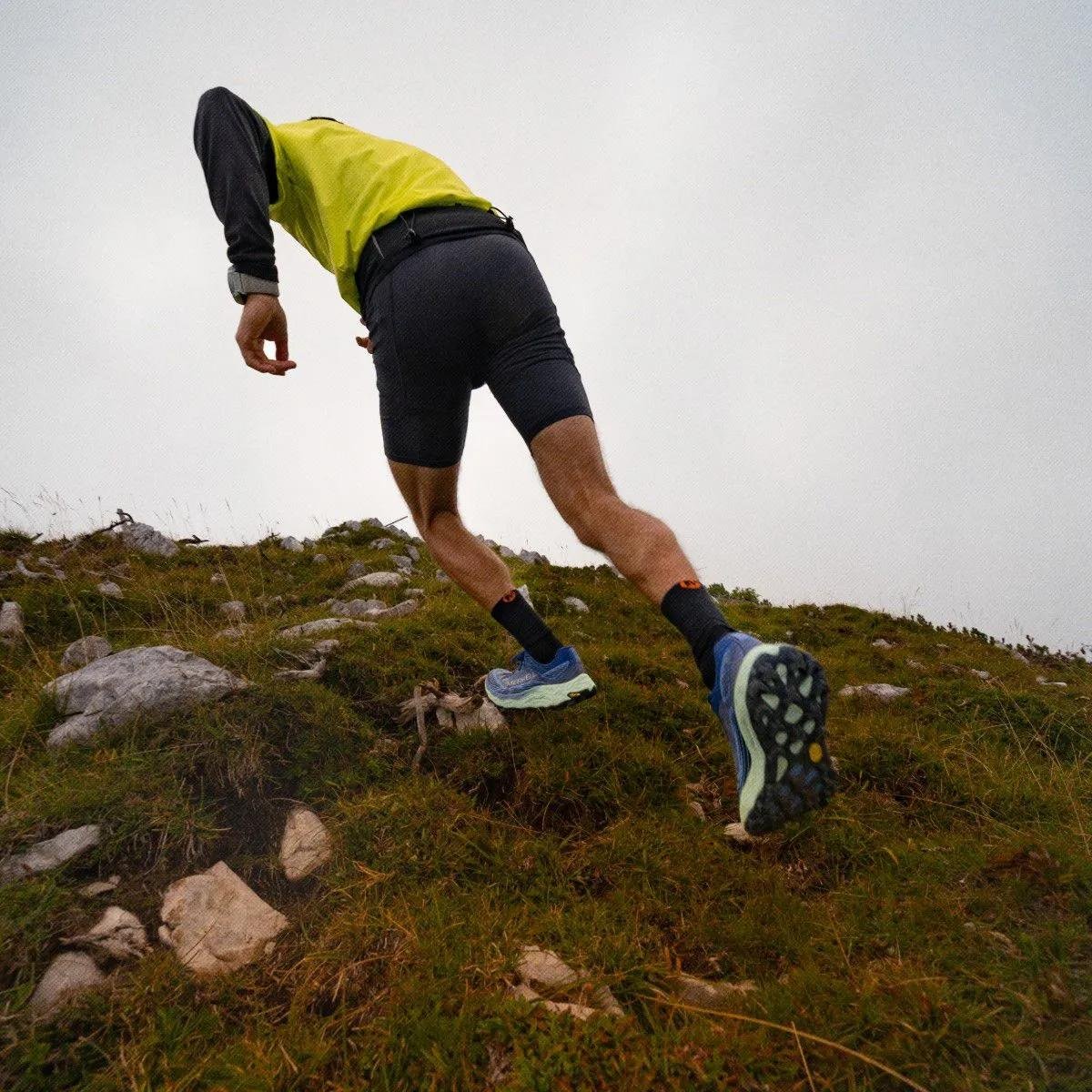 Runner sprinting up a rocky hill in profile with the sky behind them.