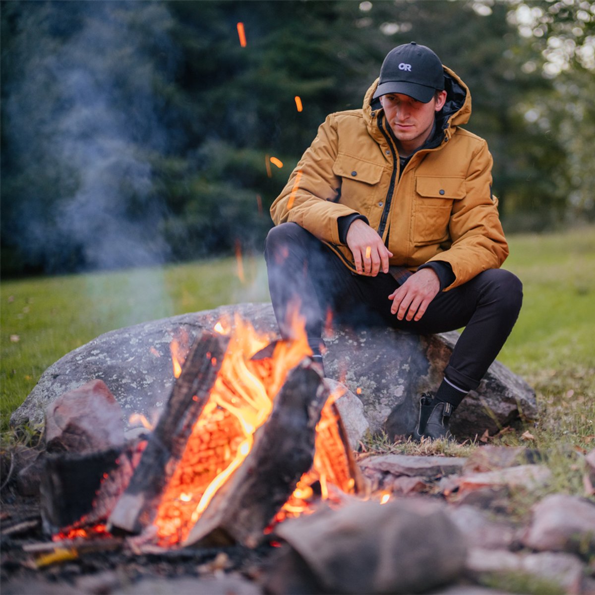 A man wears Ferrosi pants and he warms his hands by a campfire.